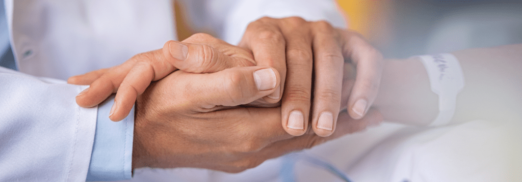 focus sur les mains d'un medecin qui tienne la main d'une personne âgée sans doute alitée à l'hôpital